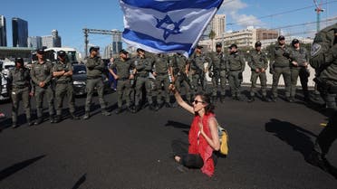 Israeli forces stand guard as a protester waves a national flag during a demonstration against the government's controversial judicial reform bill in Tel Aviv on March 9, 2023. (AFP)
