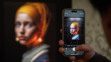 A visitor takes a picture with his mobile phone of an image designed with artificial intelligence by Berlin-based digital creator Julian van Dieken (C) inspired by Johannes Vermeer's painting Girl with a Pearl Earring at the Mauritshuis museum in The Hague on March 9, 2023.