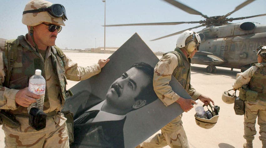 جنود أميركيون في مطار بغداد مع صورة لصدام حسين بعد إطاحة نظامه يوم 14 أبريل 2003 - فرانس برس