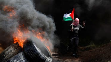 A man holds a Palestinian flag as he passes burning tires during a protest against Israeli-Palestinian meeting in Sharm el-Sheikh, at the Israel-Gaza border fence east of Gaza City, March 19, 2023. (Reuters)