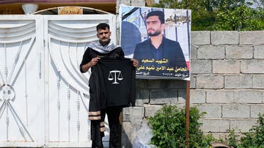 Abdullah Tamim stands next to a poster of his brother Abdel Amir Tamim while holding his brother’s graduation robe in Muqdadiyah, Iraq, Wednesday, March 22, 2023. Abdel was killed in a sniper attack earlier this month. It is not known who carried out the attack. (AP)