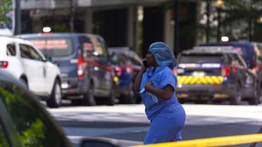 A woman in scrubs talks on the phone as police officers work the scene of a shooting at a Northside Hospital medical facility on May 3, 2023 in Atlanta, Georgia. Police say one person was killed and four others injured in the shooting and the suspect is still at large. (AFP)