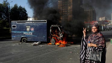 A woman gestures next to a burning police vehicle during a protest by the supporters of Pakistan’s former Prime Minister Imran Khan after his arrest, in Karachi, Pakistan, on May 9, 2023. (Reuters)