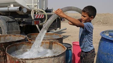 Haider Jalil, 10, fills a water tank from a truck outside his family home in the village of Al-Bouzayyat which sits on the bank of a former canal which has dried up, in Diwaniya, Iraq, October 20, 2022. (Reuters)