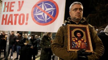 Protesters hold an anti-NATO banner as a man stands with a religious image during a demonstration against a Western-backed deal on normalizing ties between Kosovo and Serbia in Belgrade March 17, 2023. (Reuters)