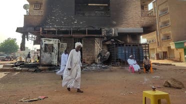 Men walk past others sitting outside a burnt-down bank branch in southern Khartoum on May 24, 2023. Sporadic artillery fire still echoed in Sudan's capital on May 24 but residents said fighting had calmed following a US and Saudi-brokered ceasefire, raising faint hopes in the embattled city. In the sixth week of war, witnesses reported a relative calm had taken hold, both in greater Khartoum and in the Darfur region's cities of Nyala and El Geneina, which have been among the other main battlegrounds. (Photo by AFP)