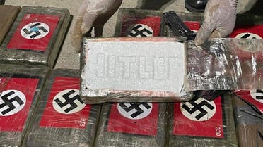 In this photo provided by the Peruvian Anti-Drug Police, an officer shows blocks of cocaine marked with Nazi swastikas and stamped with the name HITLER, at the port of Paita, Piura region, Peru, Thursday, May 25, 2023. (AP)