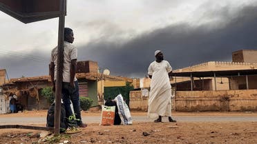 Smoke rises above buildings as people wait on the side of a road with some belongings, in Khartoum on June 10, 2023. A 24-hour ceasefire took effect on June 10 between Sudan's warring generals but, with fears running high it will collapse like its predecessors, US and Saudi mediators warn they may break off mediation efforts. (Photo by AFP)