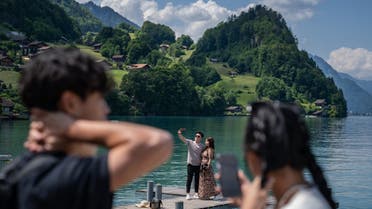 Tourists take a selfie on the famous pier seen in a popular South Korean series on Netflix, in the village of Iseltwald at the shore of Lake Brienz, in the Swiss Alps, on June 2, 2023. (AFP)