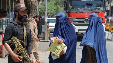 أفغانيات يمررن بالطريق بينما يقف عنصر طالبان حاملا السلاح - أفغانستان نساء طالبان - فرانس برس