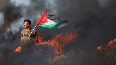 A Palestinian holds a flag as he takes part in a protest against Israeli army raid in Jenin, along Israel-Gaza border fence east of Gaza City July 3, 2023. (Reuters)