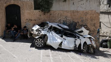 Palestinians sit behind a wrecked car in the occupied West Bank city of Jenin on July 5, 2023, after the Israeli army declared the end of a two-day military operation in the area. The Israeli military launched the raid on the Jenin refugee camp early on July 3, during which 12 Palestinians and one Israeli soldier were killed. (Photo by AHMAD GHARABLI / AFP)