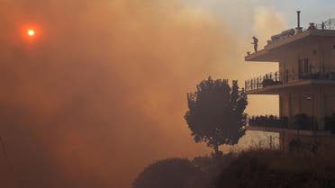 A person stands on the terrace of a house as smoke rises from a wildfire burning in Saronida, near Athens, Greece, July 17, 2023. (Reuters)
