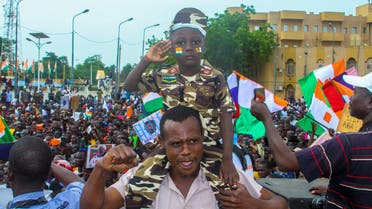 A man carries a child dressed in military uniform as he gathers with thousands of anti-sanctions protestors holding Nigerien flags and Russian flags in the capital Niamey, Niger August 20, 2023. The sign reads all the people of Niger support 100% the CNSP. REUTERS/Mahamadou Hamidou NO RESALES. NO ARCHIVES