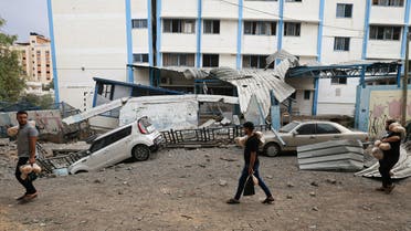 Palestinian men carrying bread walk past damaged cars and a crater in front of a school run by the United Nations Relief and Works Agency for Palestine refugees (UNRWA) following Israeli airstrikes targeting Gaza City on October 9, 2023. The Israeli army said it hit more than 500 targets in the Gaza Strip in overnight strikes, as the death toll from its war with Palestinian militants surged above 1,100. (Photo by Mahmud HAMS / AFP)