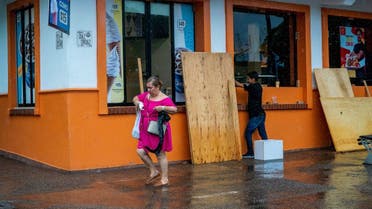A woman walks by a worker boarding up the storefront of a fast food restaurant as Hurricane Lidia barrels towards Mexico's Pacific coast, in Puerto Vallarta, Mexico October 10, 2023. (Reuters)