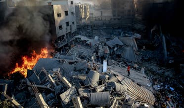  26 اکتوبر 2023 کو ایک منہدم عمارت سے دھواں اور آگ نکل رہی ہے جبکہ غزہ شہر پر اسرائیلی حملے کے نتیجے میں ہونے والی تباہی کے درمیان لوگ جمع ہیں۔ (اے ایف پی)