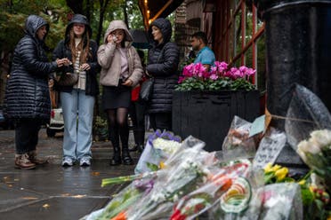 People stand before flower tributes to actor Matthew Perry outside the apartment building which was used as the exterior shot in the TV show Friends in New York on October 29, 2023. (AFP)