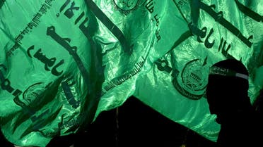 A hooded member of the Islamic militant group Hamas is silhouetted in front of Hamas flags, reading the Koran during the funeral of two Palestinian 20-year-olds in Gaza December 7, 2003. (Reuters)