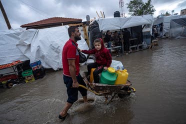 A man carries his daughter in a wheelbarrow through the flooded streets of a UN displacement camp after rainfall in the southern town of Khan Younis, Gaza Strip, Sunday, Nov. 19, 2023. (AP)