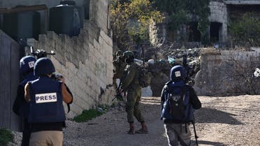 An Israeli soldier takes aim from behind a wall as journalists cover their patrol in the Jenin refugee camp, in the occupied West Bank on November 29, 2023, during an ongoing military operation in the camp. (AFP)