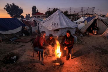 Men warm up around a fire outside one of the tents housing Palestinians displaced by the conflict in Gaza between Israel and Hamas, in Rafah in the southern Gaza Strip on December 18, 2023. (AFP)