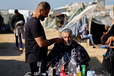 A displaced Palestinian man, who fled his home due to Israeli strikes, gets his beard trimmed in a tent camp, amid the ongoing conflict between Israel and Hamas, in Rafah, southern Gaza Strip, December 29, 2023. (Reuters)