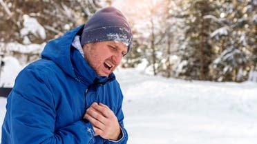 Man with chest pain suffering from heart attack while standing in snowy nature during the day. Shot of a Caucasian man holding chest in pain outdoors. Man holding chest while suffering with heartburn Man holding chest while suffering with heartburn. stock photo