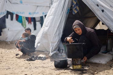 A woman cooks, as displaced Palestinians, who fled their houses due to Israeli strikes shelter in a tent camp, March 6, 2024. (File photo: Reuters)