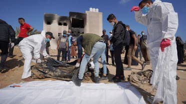 Palestinian health workers stand next to unearthed bodies buried by Israeli forces in Nasser hospital compound in Khan Yunis in the southern Gaza Strip on April 21, 2024, as battles continue between Hamas militants and Israeli forces in the besieged Palestinian territory. (AFP)