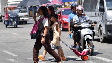A family holding umbrellas to protect themselves from the sun walk across a street in Manila on April 25, 2024.  (AFP)