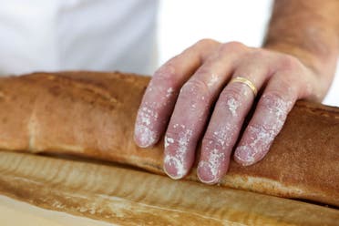 A French baker touches the baguette as he stands near a large rotating oven in an attempt to beat the world record for the longest baguette during the Suresnes Baguette Show in Suresnes near Paris, France, May 5, 2024. (Reuters)
