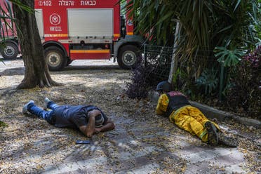 An Israeli firefighter and another Israeli man lay on the ground as a siren for incoming rockets from Lebanon into Israel goes off, amid cross-border hostilities between Hezbollah and Israeli forces, in Kiryat Shmona, northern Israel June 19, 2024. (Reuters)