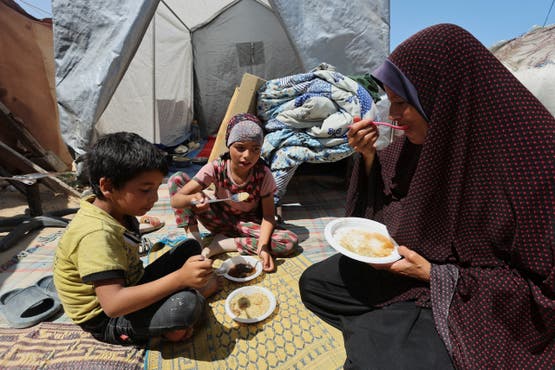 فلسطينيون صغار مع والدتهم يتناولون الطعام في خيمتهم بدير البلح وسط القطاع - 21 مايو 2025 رويترز