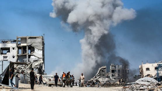 TOPSHOT - Άνθρωποι περνούν μπροστά από κατεστραμμένα κτίρια καθώς ο καπνός υψώνεται μετά από ισραηλινή επιδρομή στην Τζαμπάλια, στη βόρεια Λωρίδα της Γάζας, στις 25 Μαΐου 2025. Οι διασώστες στη Γάζα δήλωσαν ότι 22 άνθρωποι σκοτώθηκαν και δεκάδες άλλοι τραυματίστηκαν σε ισραηλινές αεροπορικές επιδρομές σε όλη την παλαιστινιακή επικράτεια στις 25 Μαΐου. (Φωτογραφία από Bashar TALEB / AFP)